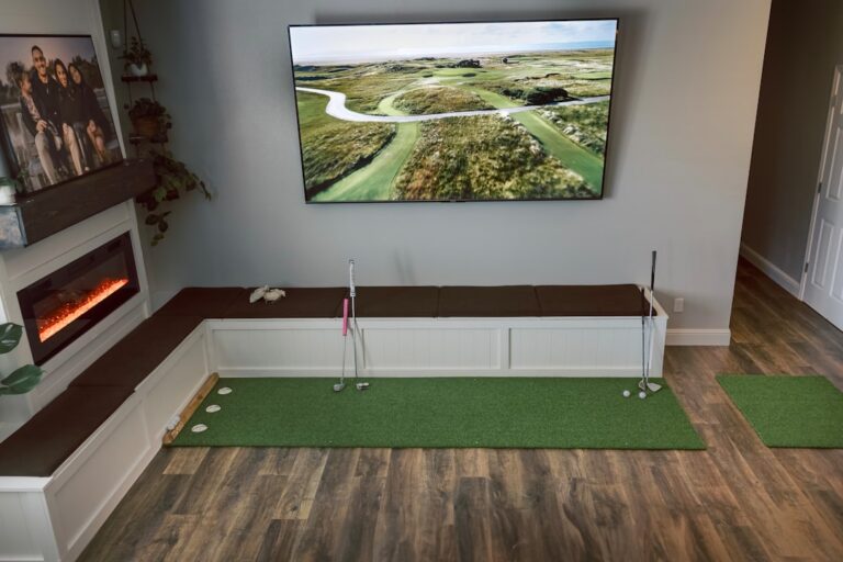 Two adults practicing golf swings on a simulator in a finished basement, with a virtual course projected on a large screen.