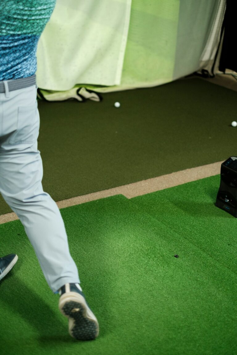Golfer practicing an iron swing indoors beside a simulator screen and launch monitor data.