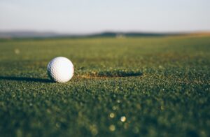 Golfers wait quietly beside a putting green while one player prepares to putt.