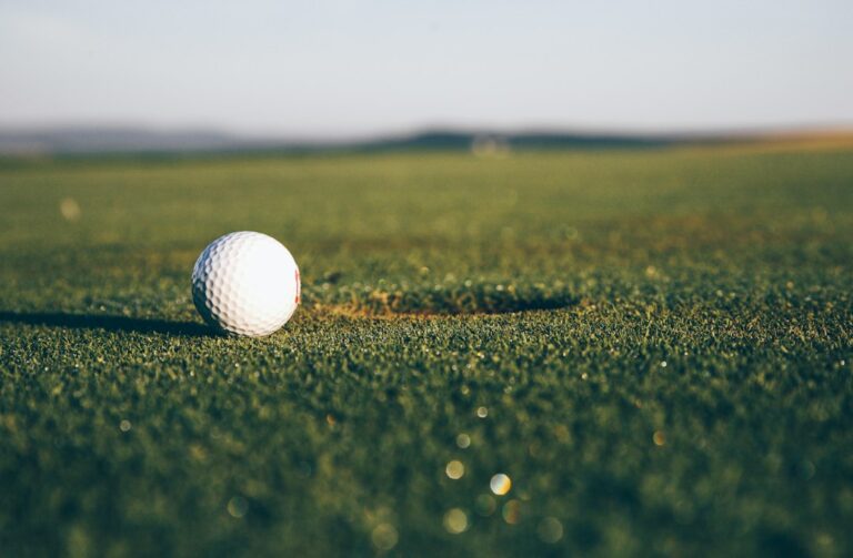Golfers wait quietly beside a putting green while one player prepares to putt.